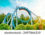 Roller coaster cart with people riding it goes through a loop upside down in green trees bushes city park. Loop metal frame of a roller coaster in an amusement park