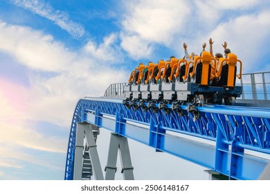 Roller coaster cart with people riding goes through the cart rises high air before descending sharply into steep dive against backdrop of blue sky clouds.