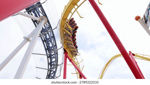 Roller coaster train speeding through loop on yellow track at amusement park. adrenaline, amusement park, thrill ride, entertainment, summer vacation, extreme fun.