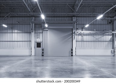 Roller Door Or Roller Shutter Using For Factory, Warehouse Or Hangar. Industrial Building Interior Consist Of Polished Concrete Floor And Closed Door For Product Display Or Industry Background.