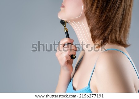Roller massager, gouache scraper, facial massage and lifting with painted surgical lines and arrows on gray background, copy space, , BeH3althy concept photo
