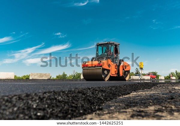 Roller rolling fresh hot asphalt on the new\
road. Road construction.