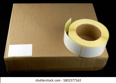 Roller of self-adhesive white stickers on a cardboard box. Cardboard box with a sticker on a black background, top view. The box is marked, a place for a label.
