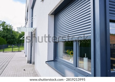 Roller shutter partly covers window on the exterior of modern house. Concept of home shading, privacy and heat protection