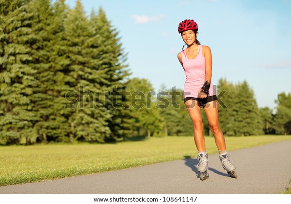 Roller skating girl in park rollerblading on\
inline skates. Mixed race Asian Chinese / Caucasian woman in\
outdoor activities.