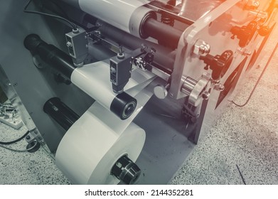 Roller of white printing paper for self-adhesive label on the shaft of the die-cutting machine in the printing house. Selective focus
