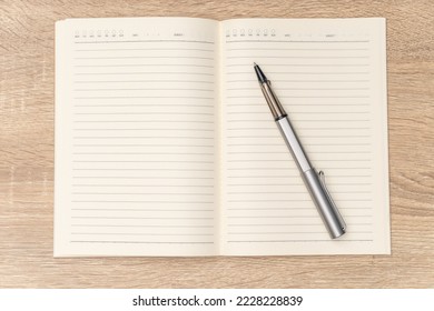 Rollerball pen is placed on the blank notebook. The notebook have lines and day boxes and subject. It seems someone is going to write the journall, diary, planner or to-do list.	