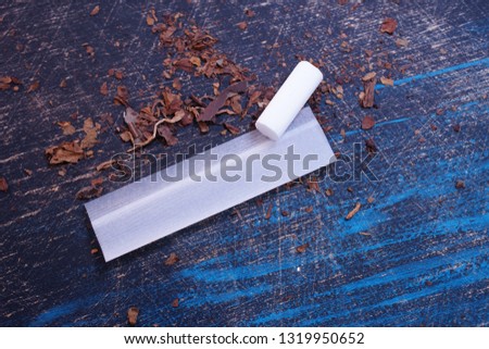 Rolling cigarette paper white filter and cut tobacco on scratched blue wooden background