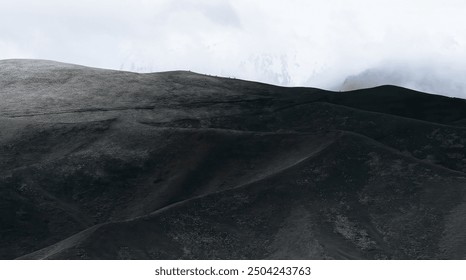 Rolling dark hills under a cloudy sky create a dramatic, moody landscape with smooth curves that blend into the misty horizon. - Powered by Shutterstock