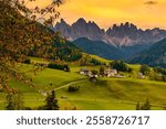 Rolling green hills blend into the majestic Dolomites, creating a breathtaking backdrop. Quaint villages dot the landscape, Santa Maddalena Val di Funes Italy Autumn season