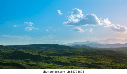 Rolling green hills under dramatic cloudy sky. Landscape capturing rolling green hills stretching toward distant mountains beneath. Fluffy clouds are evoking peace and natural beauty.