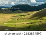 Rolling hills showing patterned fields and winding road under cloudy sky