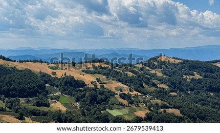 Rolling patchwork hills under a whimsical sky evoke an unexpected yearning for Lammas celebrations and rural escapades