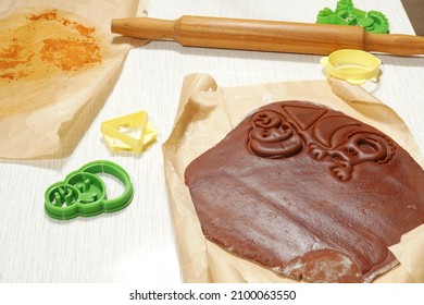 Rolling pin, cut-outs and squeezed figures of gingerbread on rolled dough.                               