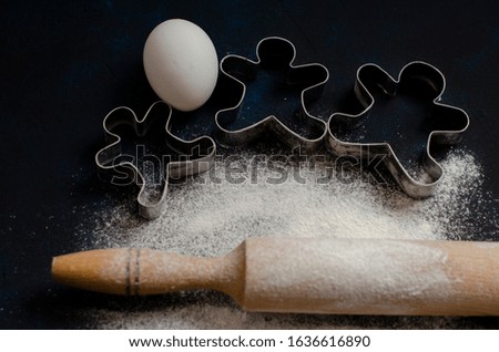 rolling pin with flour on a black background with eggs and cookie cutters. cooking cookies