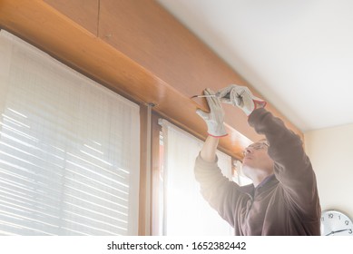 Rolling Shutter Repairer. Worker, With Gloves And Screwdriver, Adjusts A Broken Roller Shutter Of A Home. Phase Of Opening The Box Containing The Broken Roller Shutter. Selective Focus