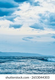 Rolling waves on open ocean with cloudy blue sky overhead