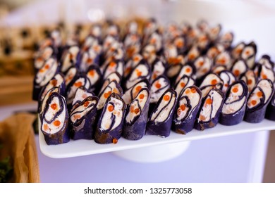 Rolls of black pancakes with cheese, salmon and red caviar on the white plate, beautiful presentation.