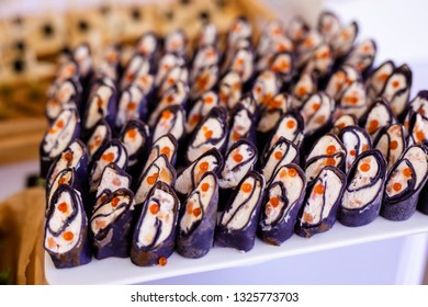 Rolls of black pancakes with cheese, salmon and red caviar on the white plate, beautiful presentation.