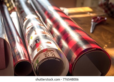 Rolls Of Christmas Wrapping Paper Laying On Table In Sunlight