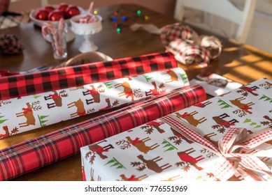 Rolls Of Christmas Wrapping Paper Laying On Table In Sunlight With Present