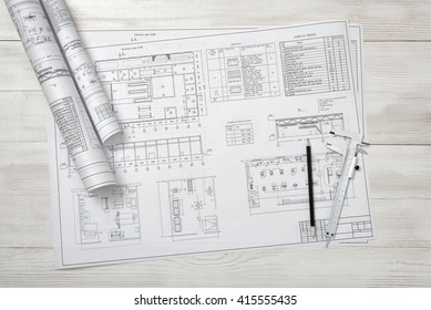 Rolls Of Drawing Sketches Lie On A Wooden Surface. Top View Compositin. Workplace Of Architect Or Constructor. Engineering Work. Construction And Architecture. Architect Drawing. Exact Calculation.