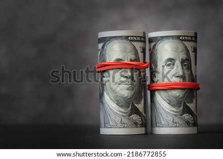 Rolls of hundred-dollar bills with red rubber bands on them, covering mouth and eyes of Franklin's image. The concept is people can turn a blind eye and remain silent for money; bribes, corruptions