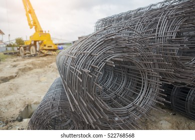 Rolls of wire mesh steel for construction put a pile on the ground, against mobile crane background. Steel wire bar in construction site.Steel reinforcement rod for concrete. Construction  concept.
