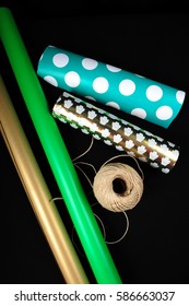 Rolls Of Wrapping Paper And Roll Of Twine On Black Surface.  High Angle View And Vertical Photo.