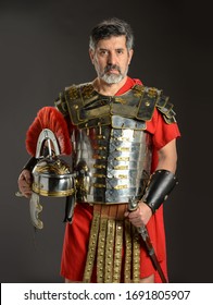 Roman soldier holding his helmet and gripping his sword on a dark background