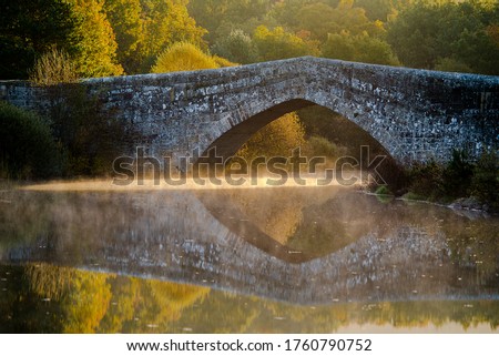 Roman stone bridge, with reflection in the water and sun rays entering from below and with fog, mist