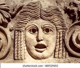 Roman Theatrical Mask Or Goddess In Greek Mythology. Ancient Mask In A Greek Theatre, Relief On Stone Wall. Decoration Of Theater For Tragedy Performance, Classic Art And Antique Culture Of Europe.