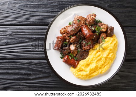 Romanian festive dish pomana porcului consisting of pieces of fried pork, sausages and offal served with corn porridge close-up on a plate on the table. Horizontal top view from above
