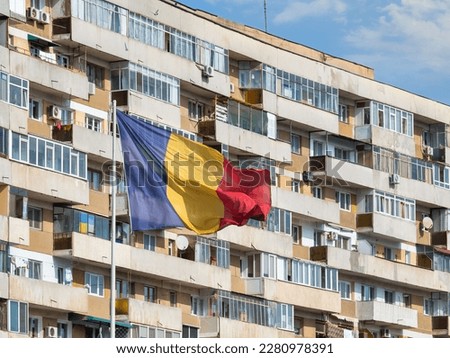 Romanian national flag in the wind and a worn out communist apartment building in the background, in Bucharest Romania.