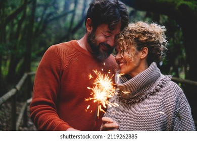 Romantic adult couple enjoy and love together with fire sparkler light in the forest green trees background. Man and woman with tenderness and relationship celebrate with firelight and smile