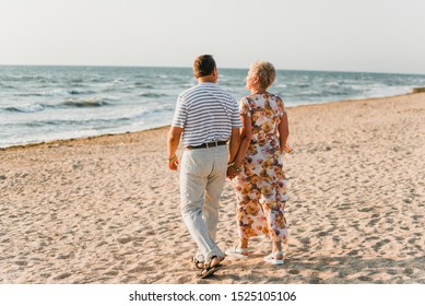 Romantic adult couple standing together on the beach. Mature pair relax at the seaside on holiday. Happy familiy walking and holding hands near sea. Husband embracing wife. Love story near the ocean