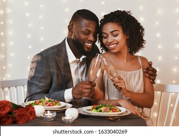 Romantic african american couple drinking champagne in fancy restaurant, having dinner with candles