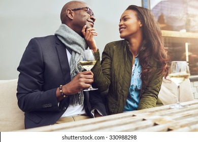 Romantic African American Couple On A Date Flirting Together At A Restaurant Table As They Enjoy A Glass Of White Wine