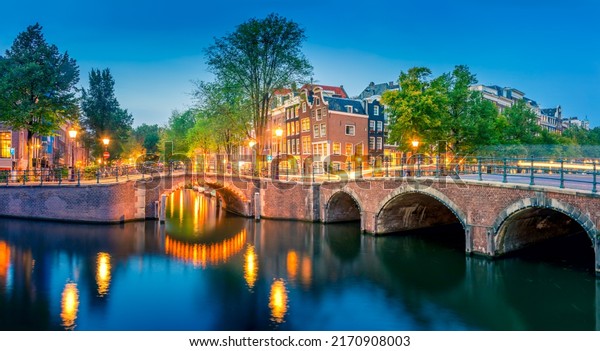 Romantic Amsterdam lit the lights. Evening\
panoramic view of the famous historic center with lantern lights,\
bridges, canals and cute Dutch houses. Amsterdam, Holland, European\
travel. Panoramic\
image