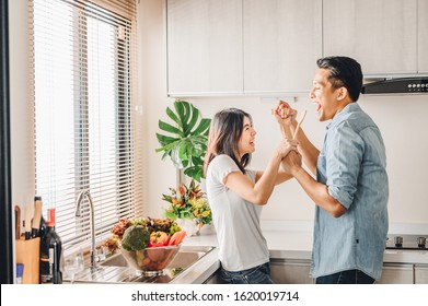 Romantic Asian couple in love is singing and dancing while cooking together in kitchen