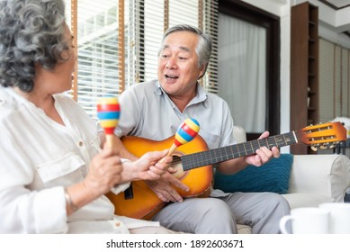 Romantic Asian Senior Couple Playing Acoustic Guitar Together. Happy GrandFather And GrandMother Singing Together At Home. Old Man And Woman Lover Having Fun With The Music And Instrument