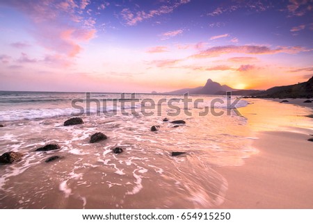 Romantic atmosphere in peaceful Sunset at Bai nhat beach Condao island-Vietnam. Taking with long exposure in the evening smooth wavy motion by Big rocks near shoreline, pink horizon with sun rays.