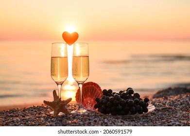 Romantic atmosphere at sunset by the sea. Heart between glasses against the background of the sun. Selective focus on starfish and left glass, narrow focus