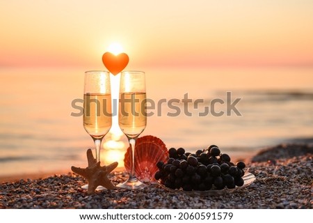 Romantic atmosphere at sunset by the sea. Heart between glasses against the background of the sun. Selective focus on starfish and left glass, narrow focus