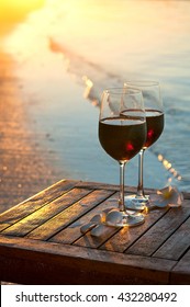 Romantic Beach Scene: Two Glasses Of Red Wine At Sunset Near Water Line