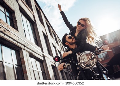 Romantic Biker Couple With Black Motorcycle. Handsome Bearded Man And Young Attractive Woman Outdoors With Cafe Racer.