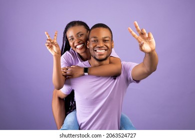 Romantic Black Couple Having Fun Together, Showing V Peace Symbol Sign Gesture With 2 Two Fingers, Cheerful African American Guy Piggybacking Happy Girlfriend, Joyful Woman Riding On Guy's Back