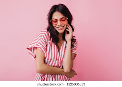 Romantic Brown-haired Girl In Trendy Heart Glasses Posing With Shy Smile. Indoor Photo Of Graceful Young Woman In Summer Attire And Accessories.