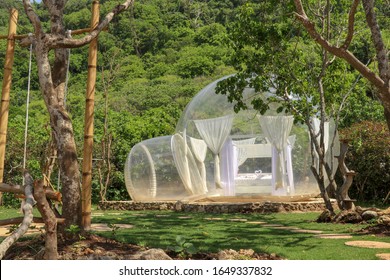 Romantic Bubble House With Transparent Walls. White Wooden Double Bed With Mosquito Net Inside Bubble. Honeymoon In An Inflatable Tent. Tourist Attraction In Tropical Paradise On Bali, Indonesia.