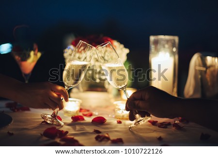 Romantic candlelight dinner for couple table setup at night. Man & Woman hold glass of Champaign. Concept for valentine's day or date.